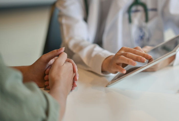 Healthcare professional showing a tablet screen to another individual sitting at the same table with them.